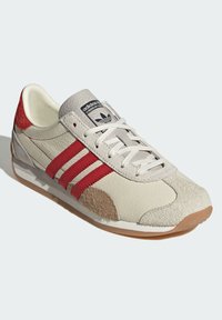 Adidas sneakers featuring a beige leather upper, red stripes, grey suede accents, and a rubber sole. Classic, retro design.