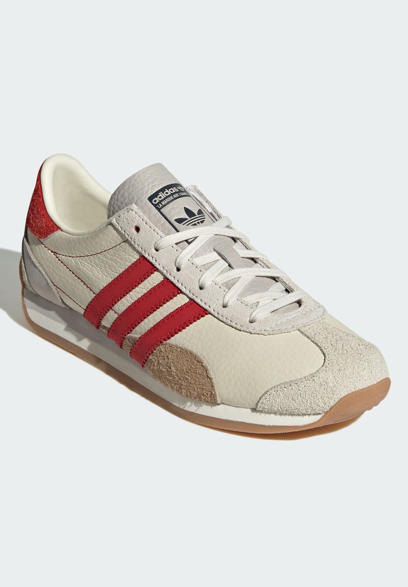 Zapatillas Adidas con parte superior de cuero beige, rayas rojas, acentos de ante gris y suela de goma. Diseño clásico y retro.