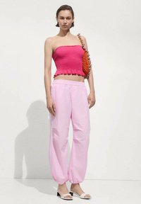 Top aderente rosa testurizzato senza spalline con orlo a volant, abbinato a pantaloni rosa larghi. Accentuato da una borsa arancione con perline e sandali bianchi.