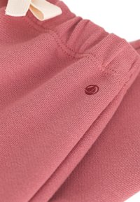 Tessuto di cotone rosa con una finitura testurizzata. Presenta una vita arricciata e un piccolo logo stampato in rosso sul lato.