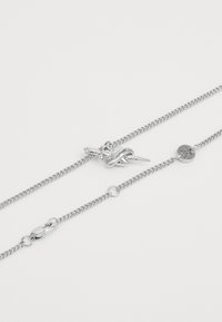 Colier din lanț argintiu cu zale, dotat cu o clemă tip homar, un charm în formă de inimă și un element decorativ împletit. Textură netedă pe toată lungimea.