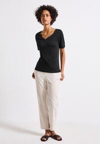 Černý krátký rukáv top s výstřihem do V a elegantním designem, spárovaný s lehkými béžovými kalhotami volného střihu a černými plochými sandály.