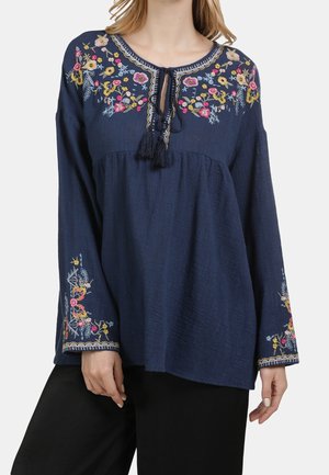 Navy blue long-sleeve blouse with multicolored floral embroidery on yoke and sleeves, featuring a tassel tie neckline.