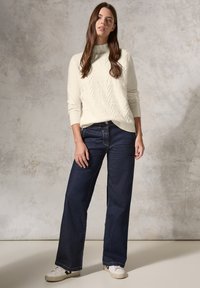 Maglione lavorato a maglia color crema con un motivo a zigzag testurizzato, abbinato a jeans scuri dal fit morbido e sneakers bianche. Look semplice e casual.