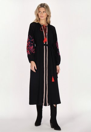 Zwart midi-jurk met lange mouwen, rode bloemenborduursels en een drawstring halslijn. Heeft een tailleband met kwastaccenten en een recht model.