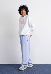 Biela mikina s ružovým logom Nike, v kombinácii s svetlomodrými teplákmi s malým modrým logom; model má na sebe strieborné tenisky.