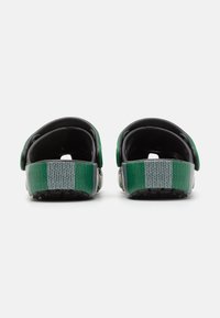 Black sandals with green straps, textured black footbed, adjustable back strap, and grey patterned sole, viewed from the rear.