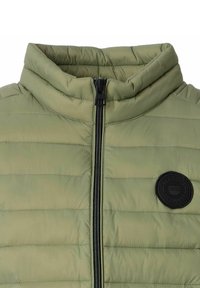 Olivgrüne Steppjacke mit hohem Kragen, horizontal gestepptem Muster, schwarzem Reißverschluss und einem runden schwarzen Logo-Patch auf der Brust.