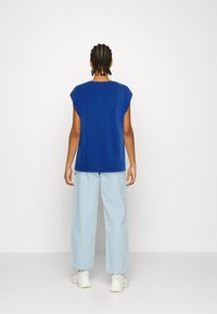 Blue sleeveless shirt with a relaxed fit, paired with light blue wide-leg jeans and white sneakers. Minimalist design, smooth texture.