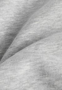 Tessuto in cotone grigio chiaro con una superficie morbida e leggermente strutturata, caratterizzato da un sottile motivo melangiato e delicate pieghe.