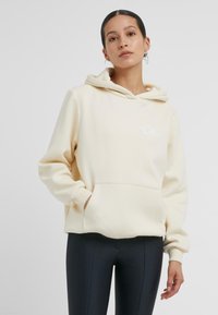Cremfarbener Hoodie aus weichem Stoff, mit einer Kängurutasche und einer Kapuze mit Kordelzug. Auf der Brust befindet sich weißer, geschwungener Text mit der Aufschrift "Good Vibes".