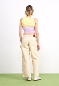 Un crop top côtelé violet clair et jaune associé à un pantalon large crème ; présente des détails de poches arrière et des chaussures claires avec des accents bleus.
