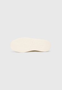 Semelle de sneaker couleur crème avec motif texturé, présentant des motifs en chevrons et de petites grips rectangulaires pour une adhérence optimale. Finition douce, design minimaliste.