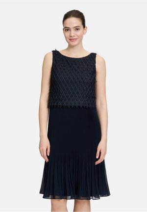 Dunkelblaues Kleid mit einem strukturierten Cropped-Oberteil mit geometrischem Muster, fließendem Faltenrock und ärmellosem Design.