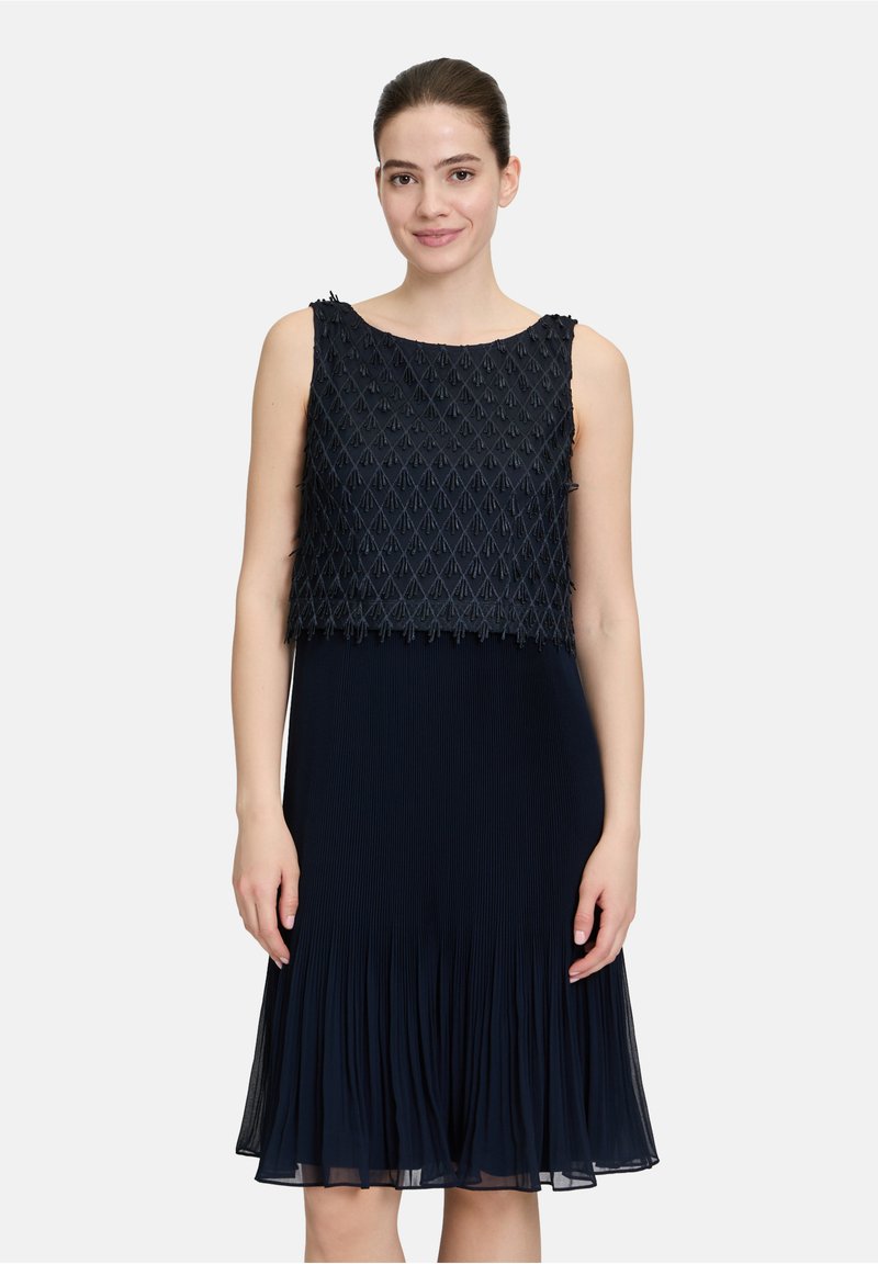 Robe bleu marine avec un haut court texturé présentant un motif géométrique, une jupe plissée fluide et une conception sans manches.