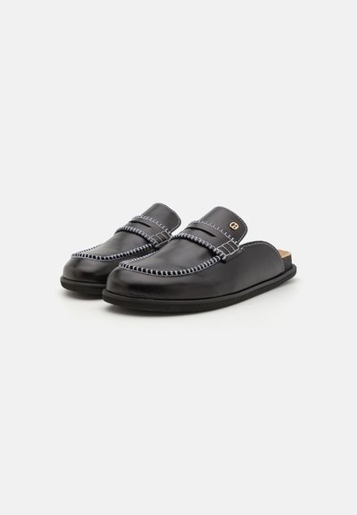 Scarpe slip-on in pelle nera con cuciture a contrasto, suola piatta e design a punta rotonda. Presentano una fascia in pelle e un accento dorato.