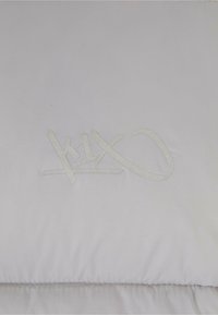 Lenjerie de pat albă cu o textură netedă, având un logo subtil embosat în gri deschis. Designul include cusături pe margini.