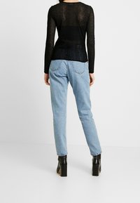 Svart långärmad topp med ett tunt, mönstrat tyg, kombinerad med ljusblå högmidjade jeans och svarta ankelboots med klack.