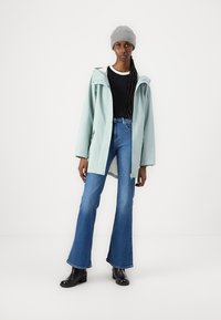 Lys myntegrønn vanntett jakke med hette, sammen med høy midje blå flare jeans og svarte ankelstøvler. Strikket grå lue.