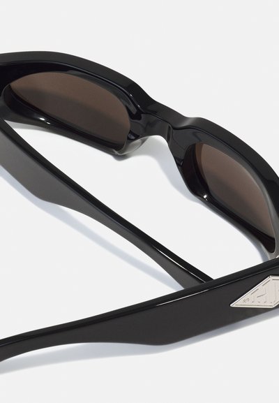 Ochelari de soare negri cu o finisare lucioasă, lentile închise la culoare și un design de cadru unghiular distinctiv. Prezintă un accent argintiu pe frunză.