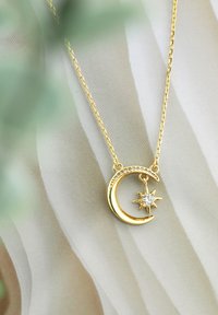 Guldhalskæde med en halvmåneanhænger prydet med små klare sten og en stjernecharme, hængende fra en delikat kæde.