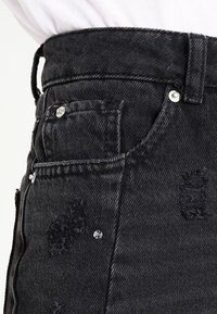 Svart jeanskjol med hög midja, fickdetaljer, slitna textur, silverfärgade beslag och dekorativa strassstenar.