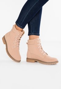 Ljust rosa snörade ankelstövlar med vadderad krage och subtil blomsterprägling, bärs med mörkblå skinny jeans.