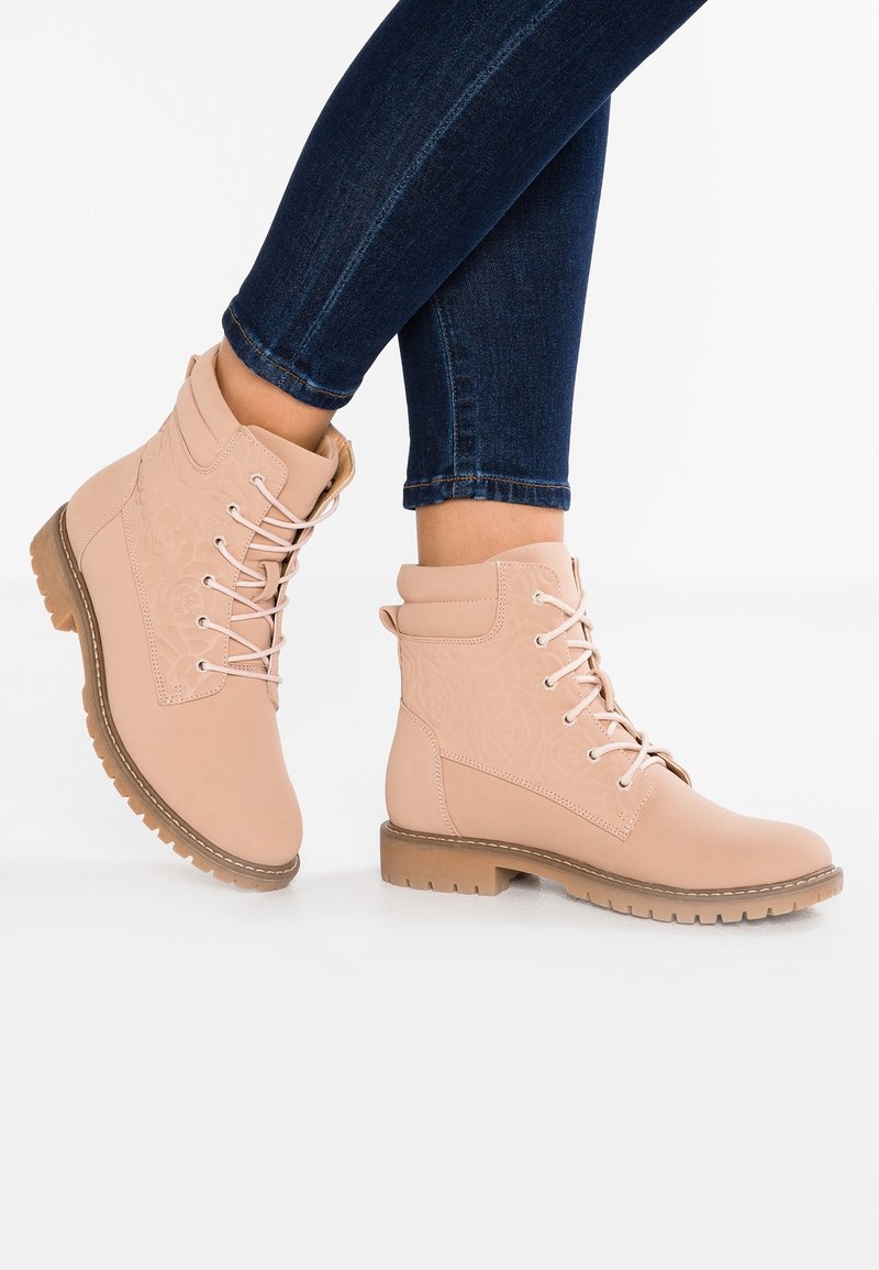 Ljust rosa snörade ankelstövlar med vadderad krage och subtil blomsterprägling, bärs med mörkblå skinny jeans.