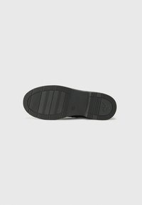 Suola di scarpa nera con una superficie testurizzata caratterizzata da scanalature orizzontali e verticali. Il logo CK è impresso nell'area del tallone.