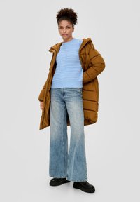 Bruine pufferjack, lichtblauwe gestructureerde trui, wijdvallende blauwe jeans en zwarte plateau-schoenen. Strakke pasvorm met prominente laagjes.