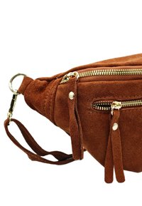 Sac banane en suede brun avec des zips dorés, plusieurs poches et une sangle pour poignet ; présente une finition texturée et des accents de franges décoratifs.