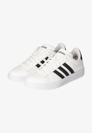 Zapatillas deportivas blancas hechas de material sintético, con un diseño de tres rayas negras, sistema de cordones en la parte delantera y suela de goma blanca.