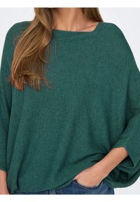 Türkisfarbener, gerippter Strickpullover mit weitem Ausschnitt und übergroßen Ärmeln, der eine lockere Passform und eine weiche Textur aufweist. Wird über Jeans getragen.