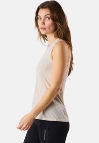 Light beige sleeveless athletic top, featuring a textured fabric, round neckline, and slim fit, paired with black fitted pants.