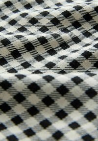 Nahaufnahme eines schwarz-weiß karierten Stoffes mit gewebter Textur und rautenförmigem Muster, der sanfte Falten und Schatten zeigt.