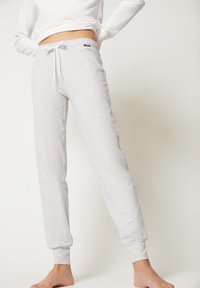 Lichtgrijze sweatpants van zacht materiaal, met een verstelbare tailleband, aangesloten boorden en zijzakken. Subtiele textuurdetails aanwezig.