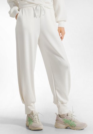 Witte, losse joggers met elastische boorden en een trekkoord in de taille, gecombineerd met beige sneakers met groene accenten.