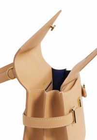 Bolso de mano de cuero beige con un diseño estructurado, detalles en hardware dorado y una parte superior abierta que revela un forro interior azul y un slot para tarjetas.