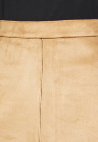 Falda de ante color beige con una textura suave, que presenta una cintura cosida y una costura central que corre verticalmente. Diseño simple sin adornos.