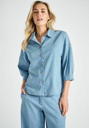 Lichtblauw denimshirt met een knoopsluiting aan de voorkant, een puntige kraag en driekwart mouwen, voorzien van houten knopen en een losse pasvorm.