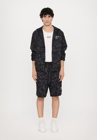 Black leopard-print tracksuit featuring a zip-up jacket and matching shorts. The fabric appears lightweight with a matte texture.