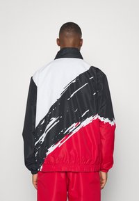 Vindjakke med farveblokdesign i sort, hvid og rød, med et markant penselstræk mønster og en elastisk kant.