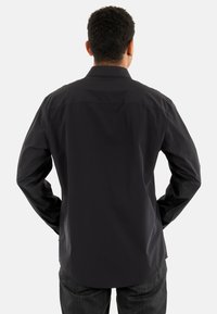 Vista trasera de una camisa negra de manga larga con botón, hecha de un material suave con cuello clásico y corte relajado, combinada con unos jeans oscuros.