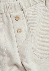 Beige katoenen broek met ribbeltextuur, twee houten knopen en zijzakken met een gladde afwerking.
