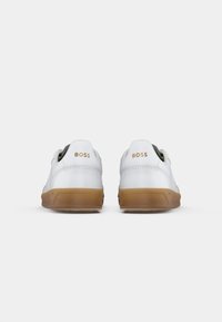 Adidași albi cu un superior din piele netedă, călcâi întărit și talpă din cauciuc bej. Logo-ul "BOSS" în aur pe călcâi. Design rotund.