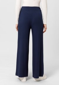 Pantalones de pierna ancha en azul marino con textura de canalé vertical, cintura alta y un acabado suave. Combinados con zapatillas blancas de corte bajo para crear contraste.