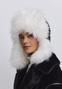 Zwarte nepbont hoed met een pluche witte bontafwerking. Heeft een volle snit en een zachte textuur, wat zorgt voor warmte en bedekking rond het gezicht.