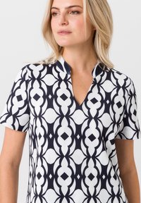 Korte mouwen top met een marineblauw en wit geometrisch patroon, met een V-halslijn en een gladde, lichte stof.