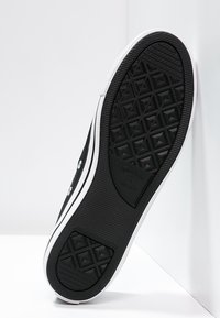 Baskets noires avec une semelle en caoutchouc texturée à motif en diamant, des accents blancs le long des bords, des œillets métalliques et des lacets plats.