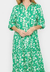 Grön blommig skjortklänning med korta ärmar, knapplist fram, tredelad kjoldesign och en mjuk textur med vita blommönster genomgående.